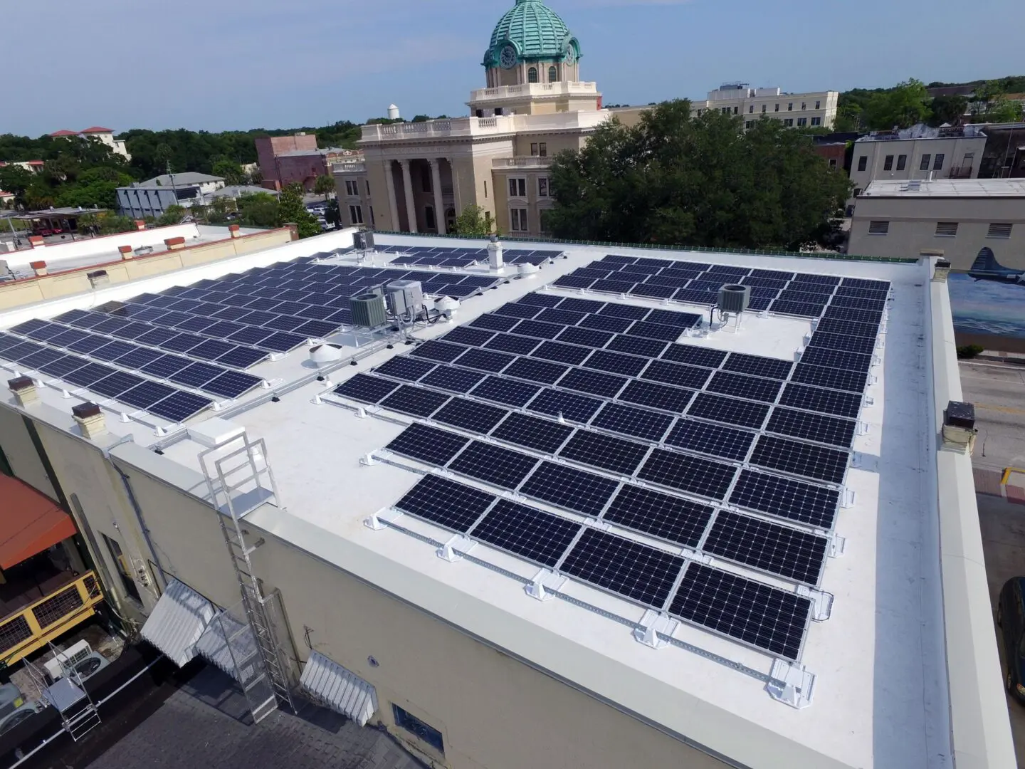Rooftop solar panels on a flat building in an urban area with a domed structure in the background.