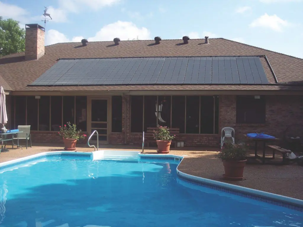 Backyard view of a house with solar panels on the roof, a swimming pool in the foreground, and patio furniture on the deck.