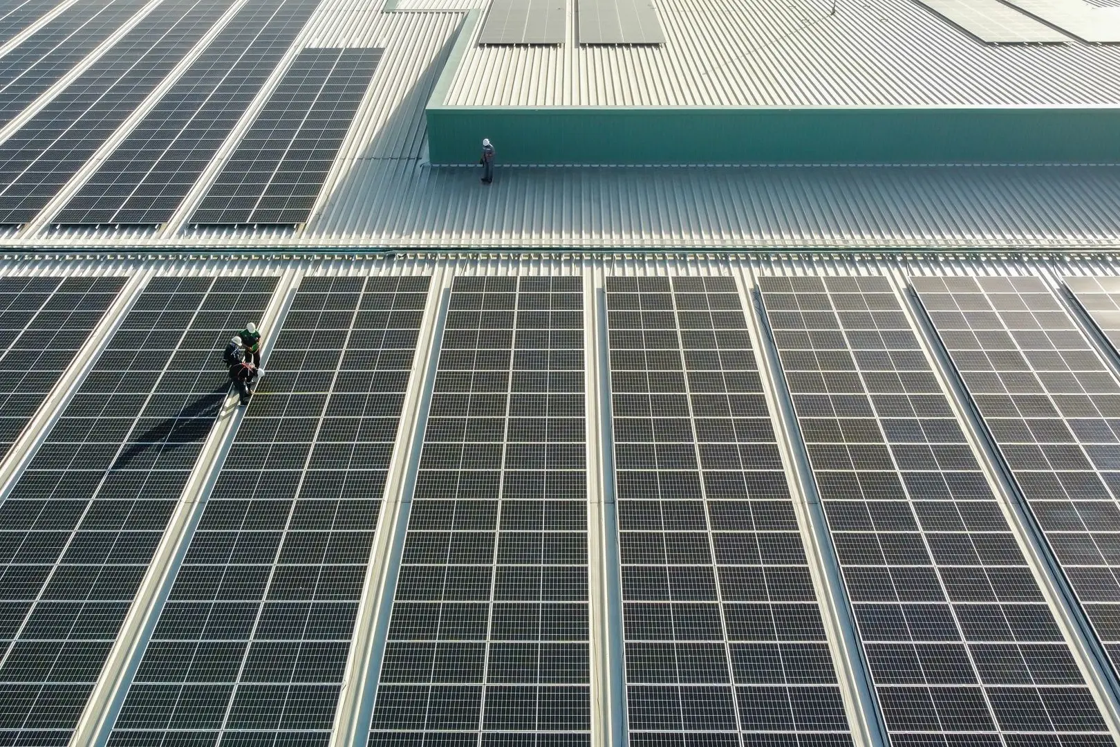Rooftop solar panels with two workers inspecting the installation on a large metal roof.