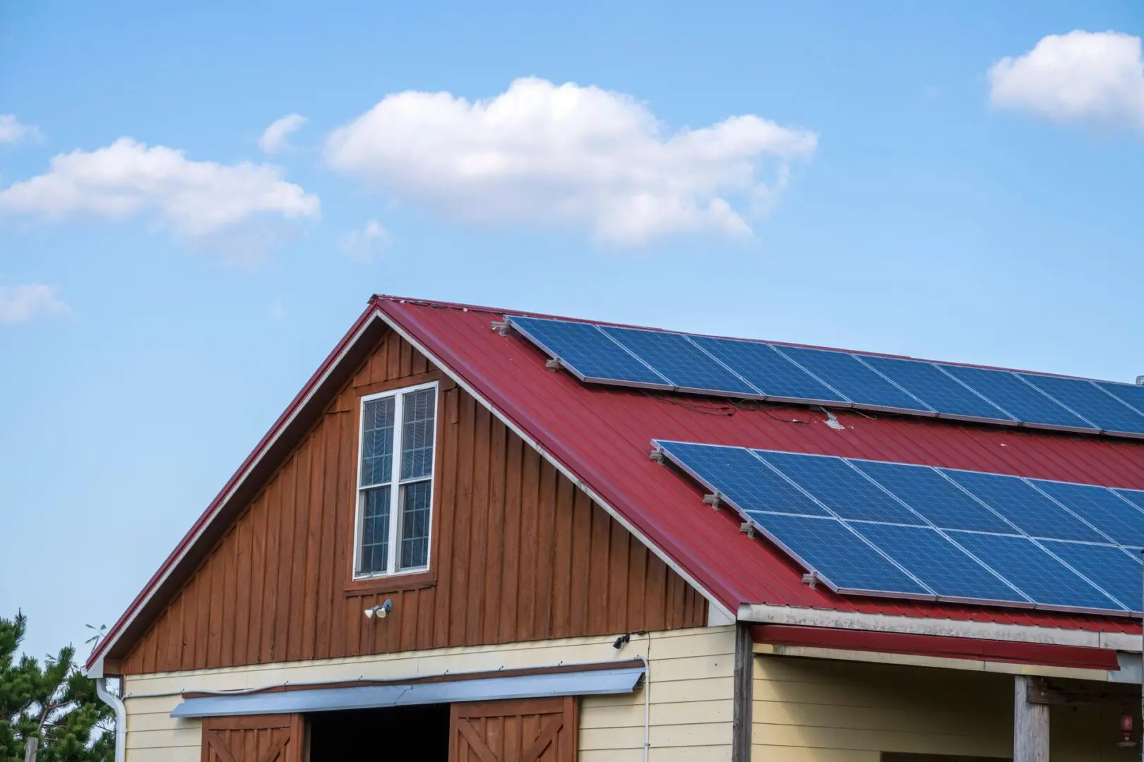 Red-roofed barn with solar panels under a blue sky with a few clouds.