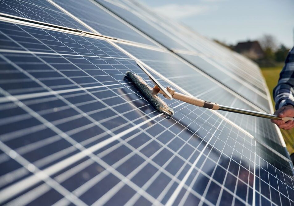 Person cleaning large solar panels with a brush on a sunny day.