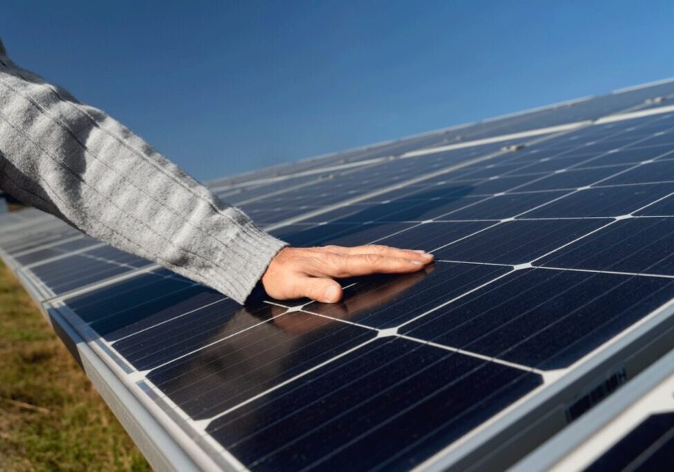 A person touches a solar panel with one hand under a clear blue sky.