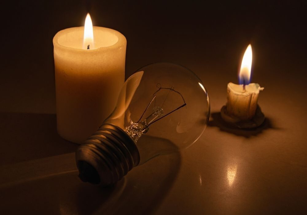 Two lit candles and an unlit light bulb rest on a surface, casting a warm glow.