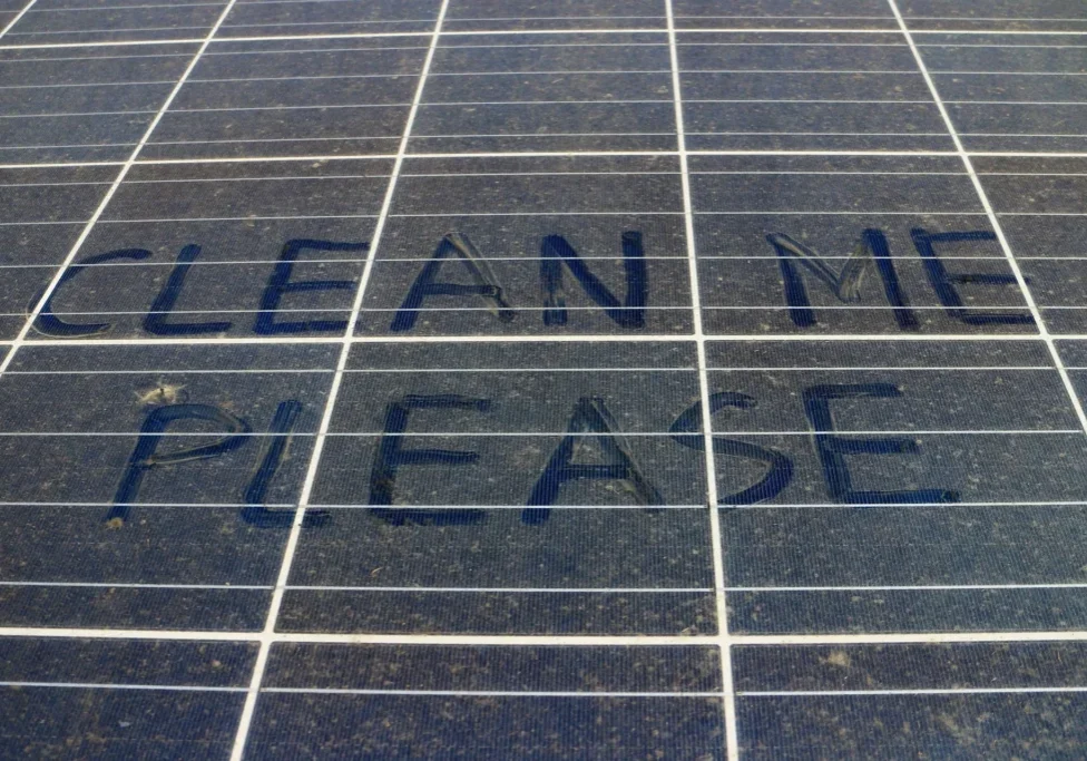 Dusty solar panel with "CLEAN ME PLEASE" written in the dirt.