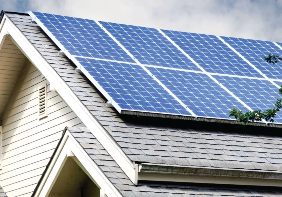 Solar panels installed on a sloped residential roof with gray shingles, under a partly cloudy sky.