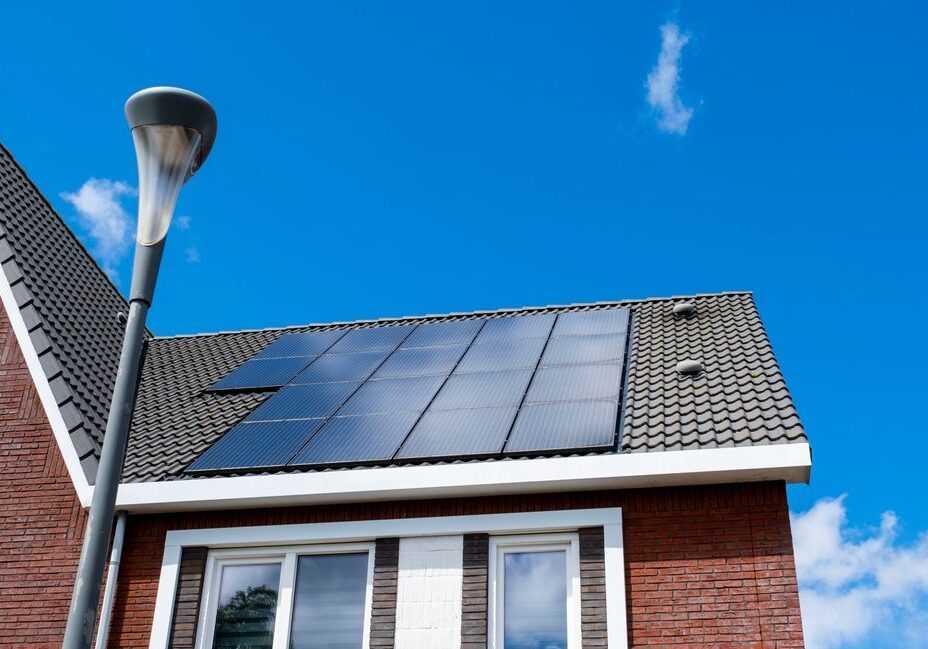 Rooftop with solar panels on a brick house under a clear blue sky, next to a street lamp.